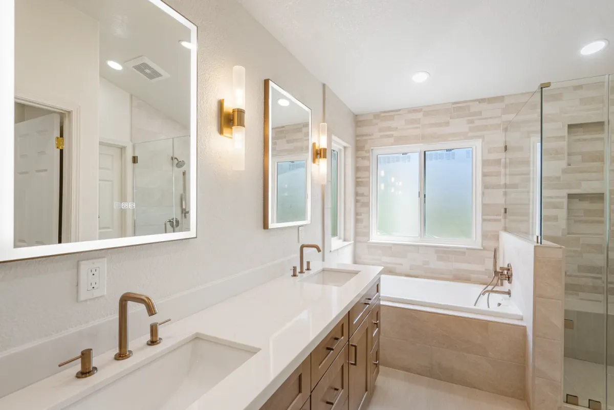 Double vanity with brass faucets and sconces, the tub and glass shower beyond