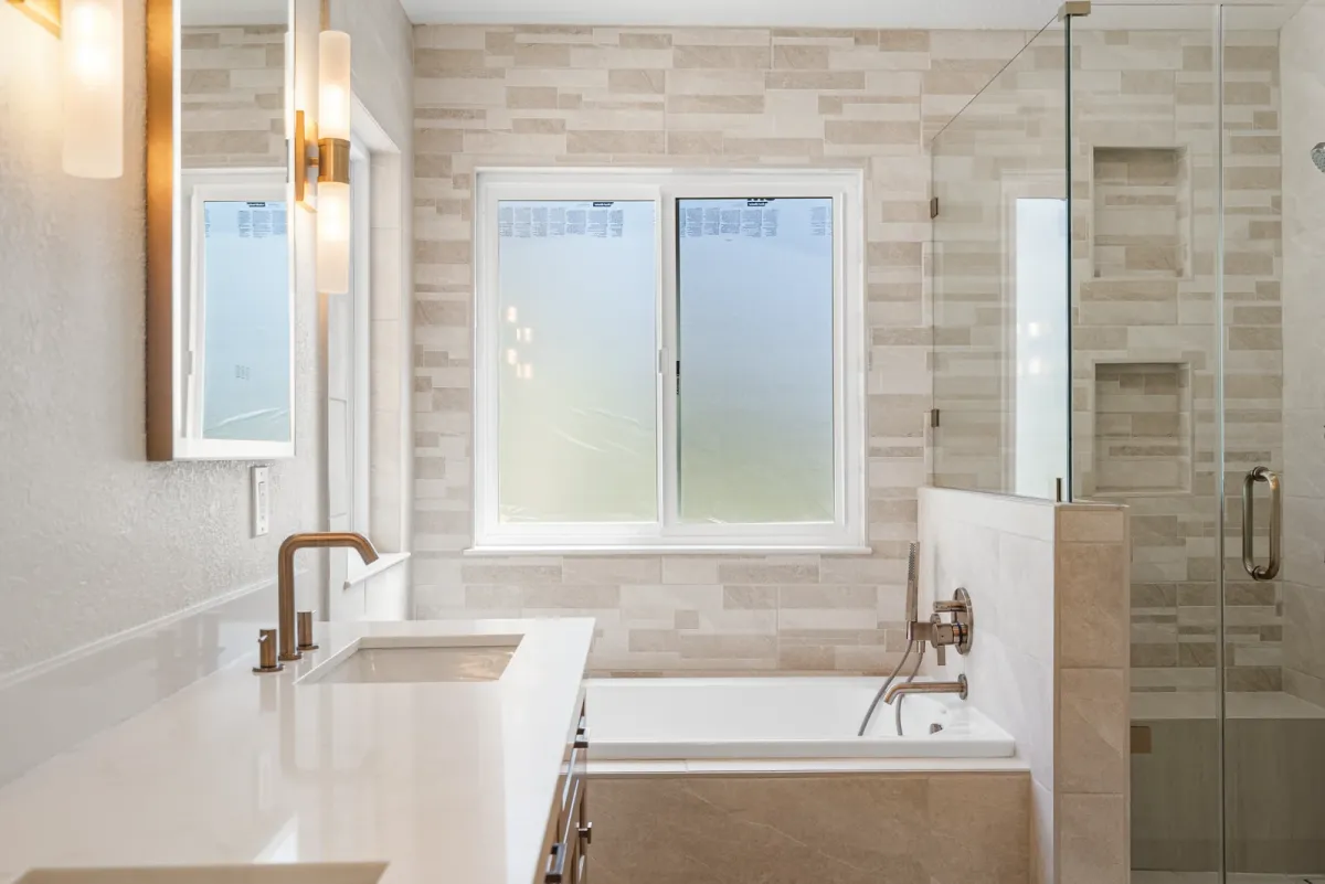 Soaking tub under a window with a brass filler and stone-look plank tile