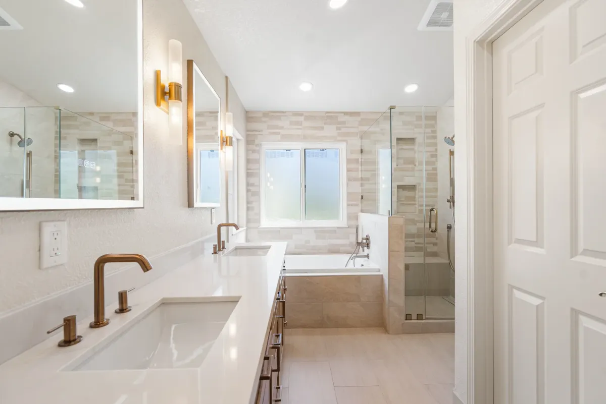 Long vanity run with brass fixtures, the tub and shower at the far end