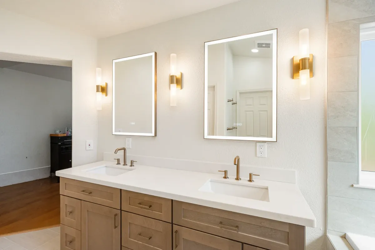 Double vanity with lit rectangular mirrors and brass sconces between them