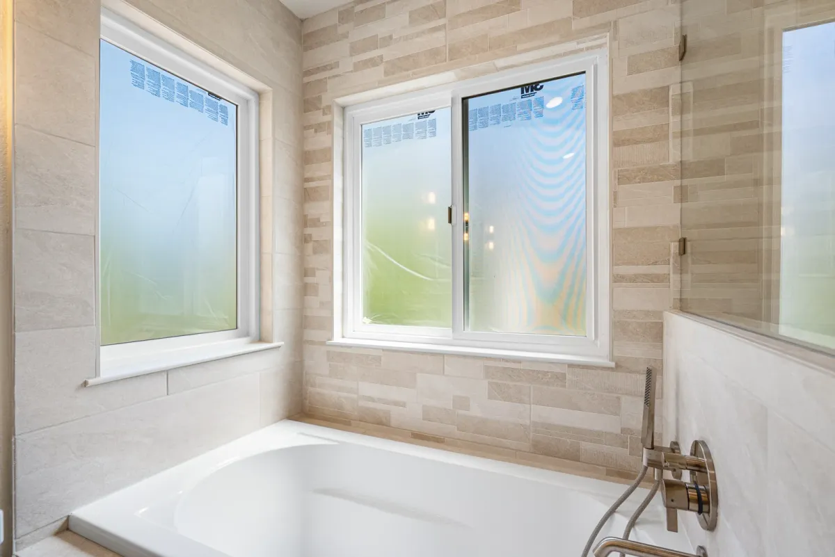 Soaking tub in a stone-tiled corner under two windows