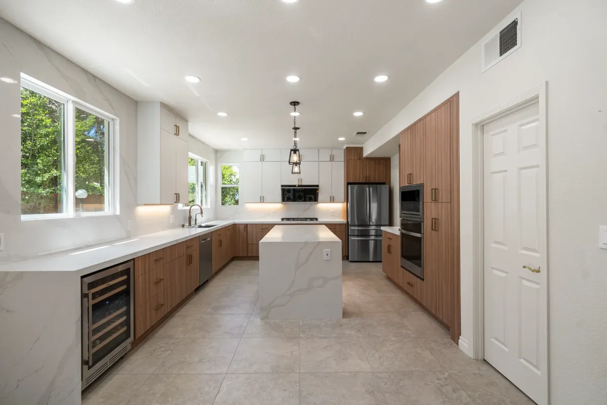 Galley kitchen with walnut base cabinets, white uppers, a waterfall quartz island, wine fridge and wall ovens