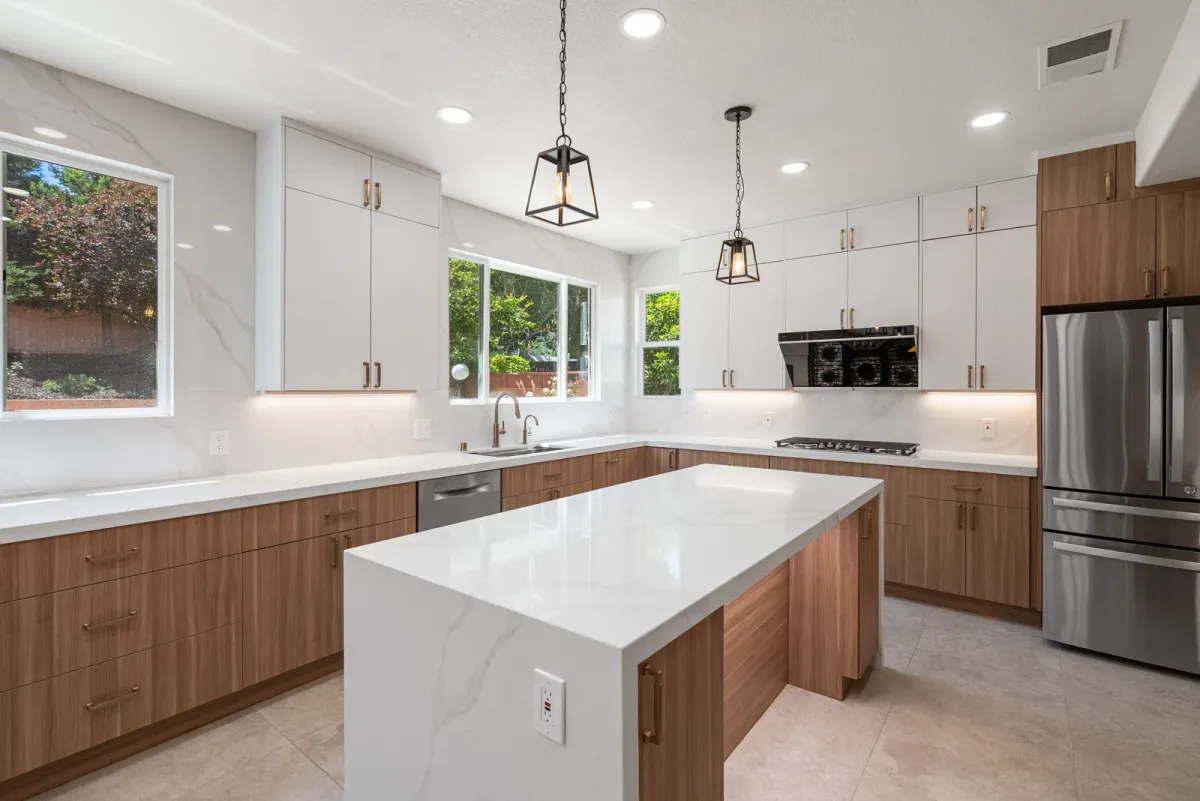 Waterfall quartz island under lantern pendants, with a window over the sink and a gas cooktop
