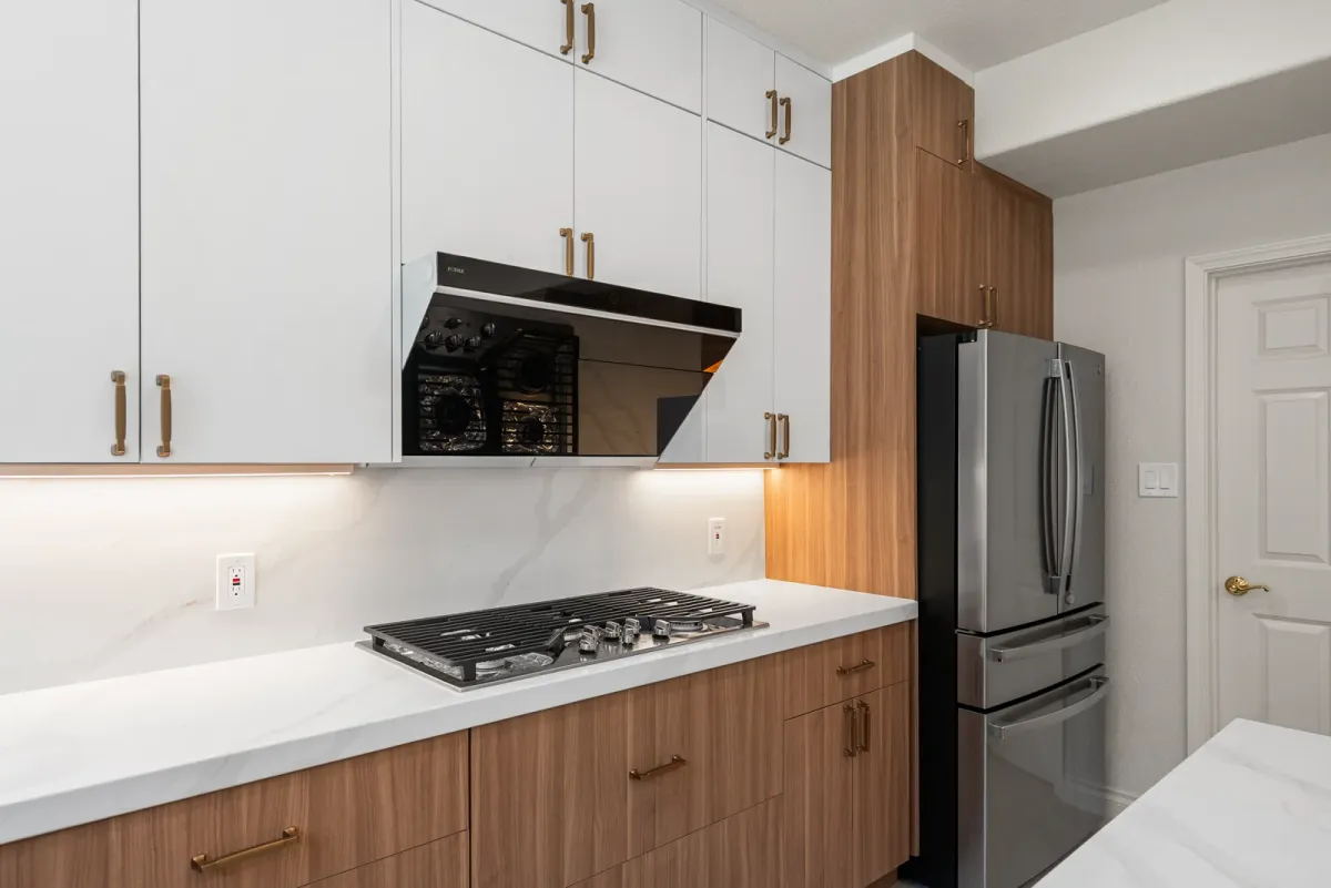 Cooktop and black hood insert between white upper cabinets and walnut base cabinets