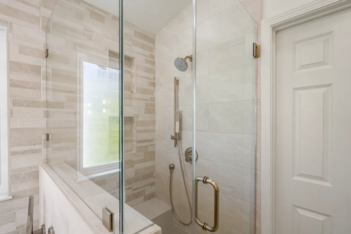 Glass shower enclosure with brass fittings beside the tub