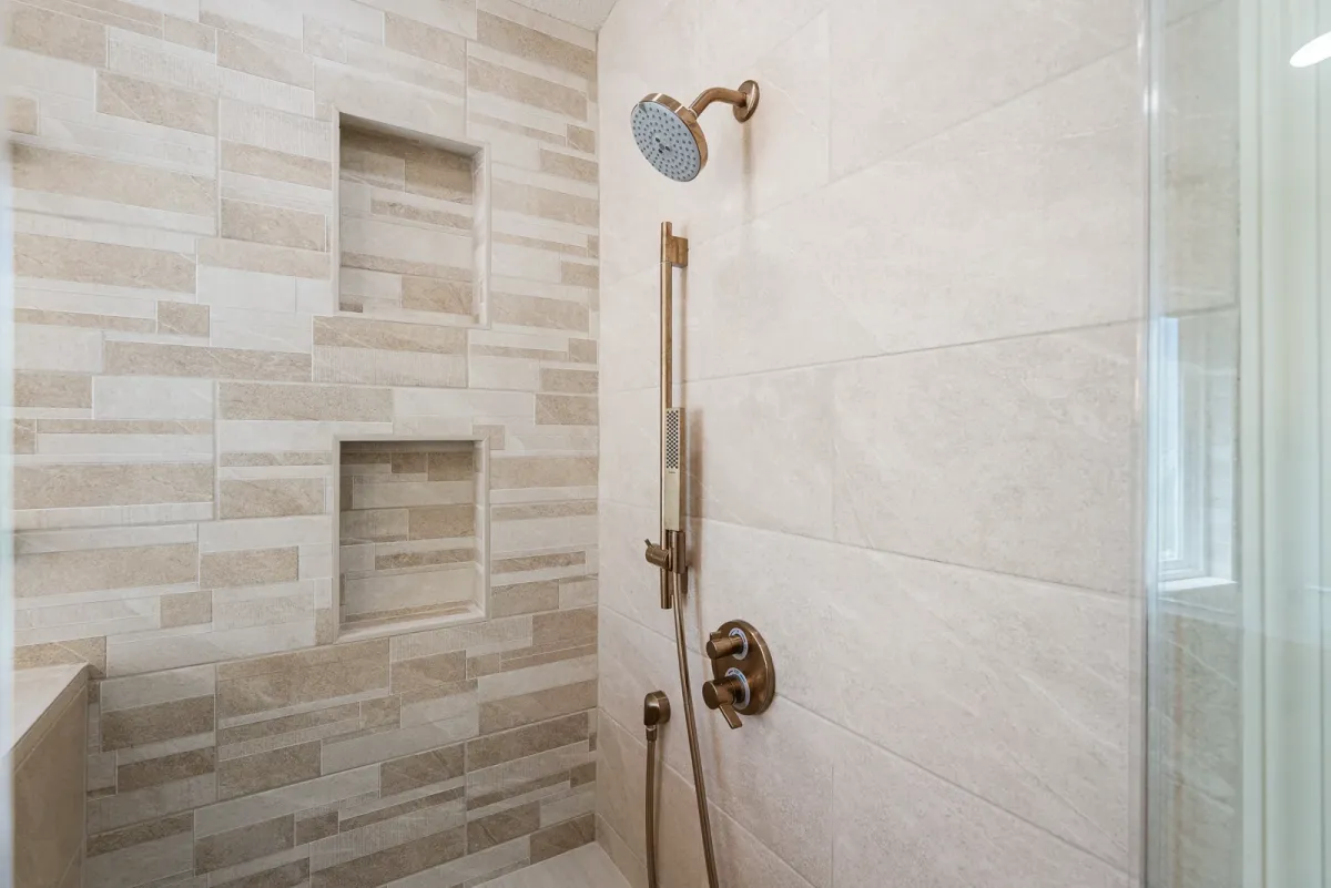 Shower wall in stone-look tile with two niches, a rain head and a handheld on a brass slide bar