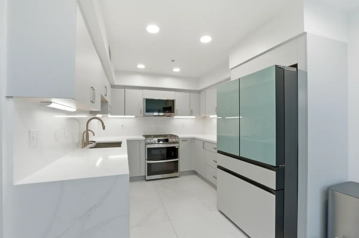 Light grey slab cabinets with a brass gooseneck faucet and a sea-green glass-panel refrigerator