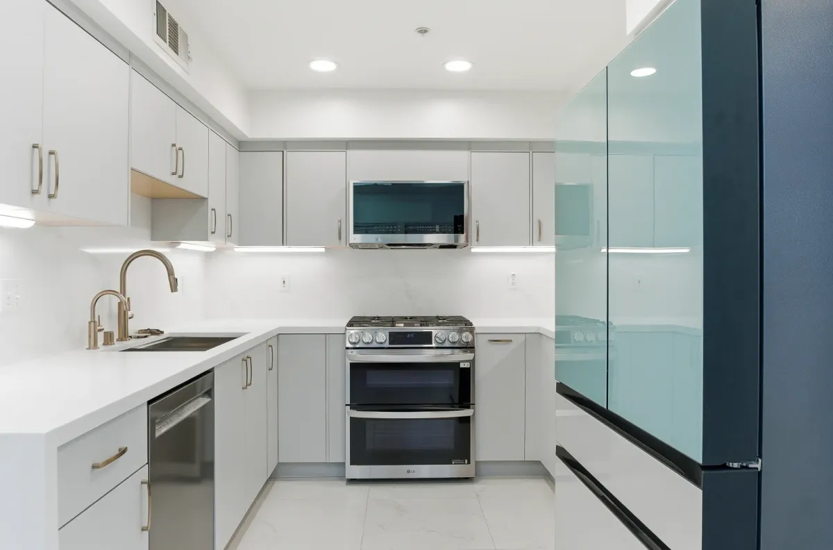 Gas range with a double oven and microwave between grey cabinets, sink with a brass faucet