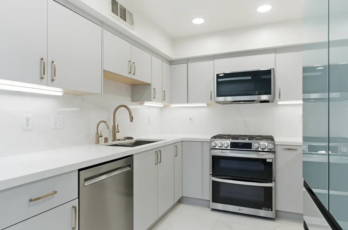 Grey L-shaped cabinet run with a slide-in range, dishwasher and brass pulls