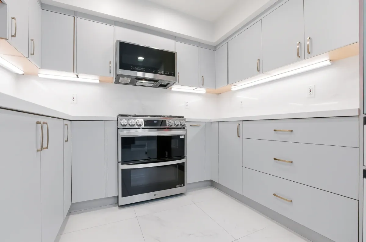 Range and microwave in the corner of the grey cabinet run with brass pulls