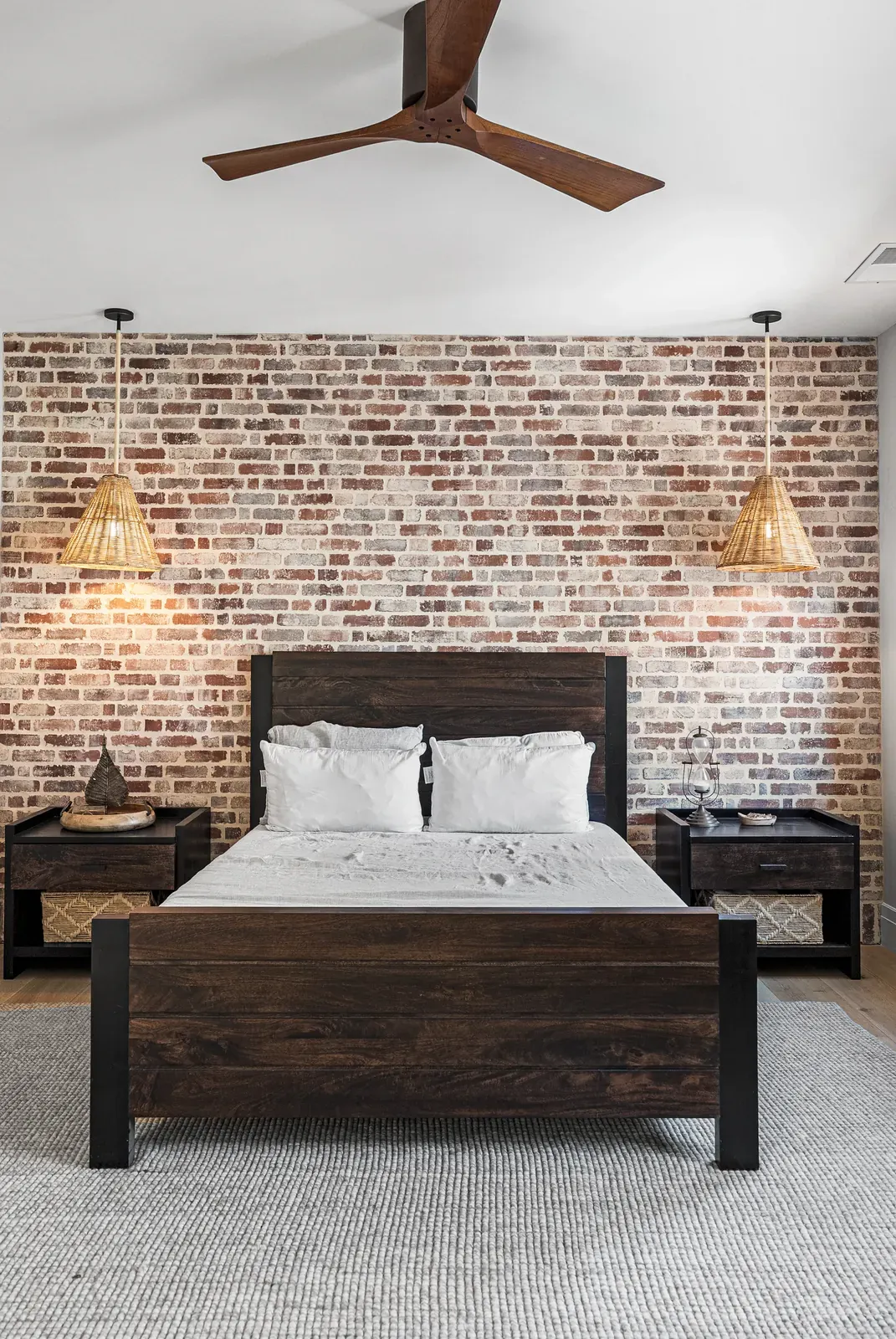 Bedroom with reclaimed brick accent wall, woven pendants and dark wood bed