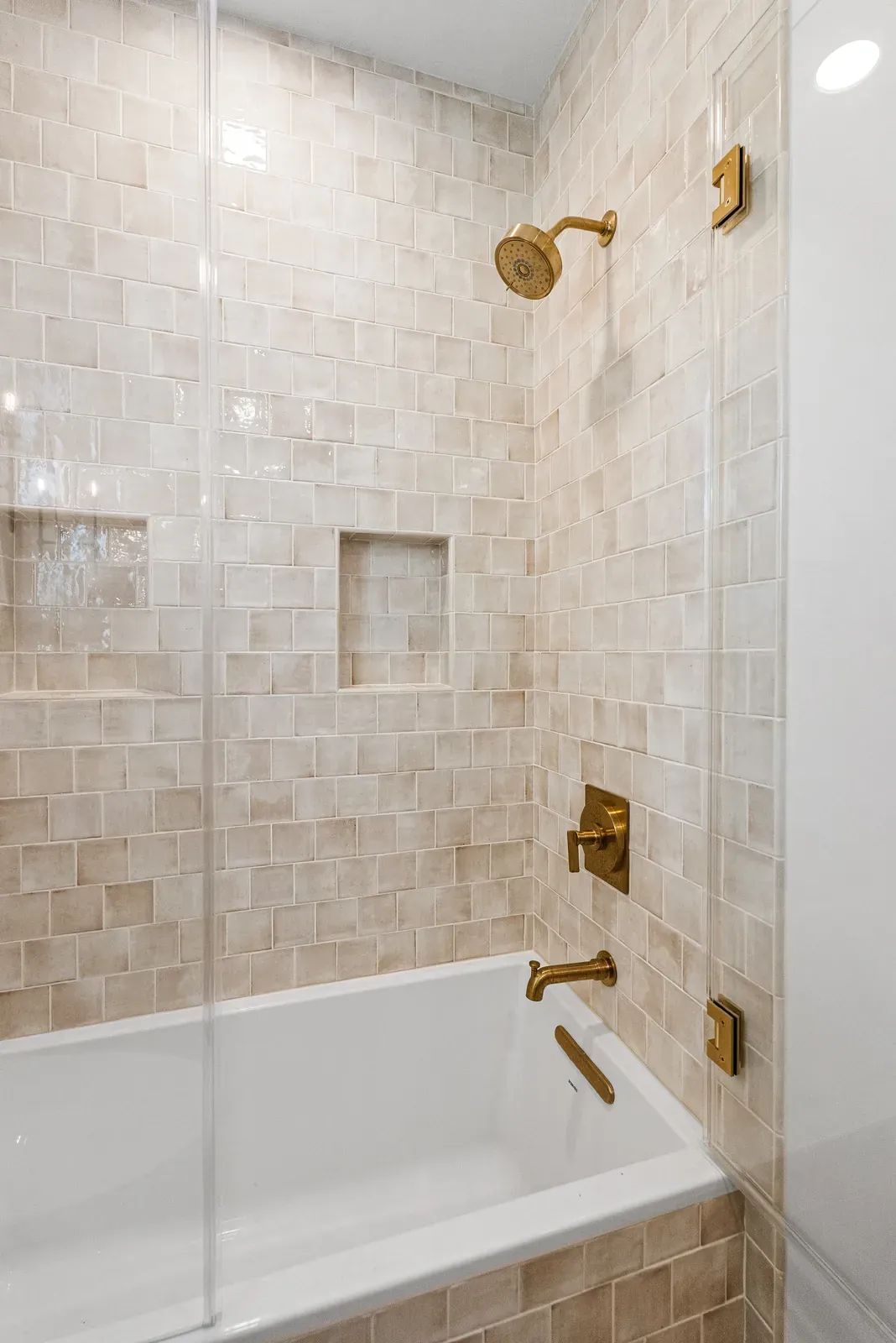 Tub and shower surround in warm zellige tile with brass fixtures