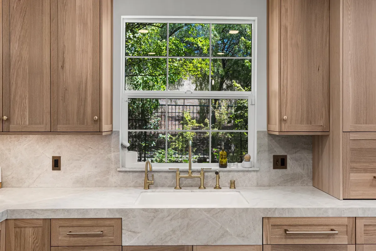 Kitchen window with unlacquered brass bridge faucet and stone sill
