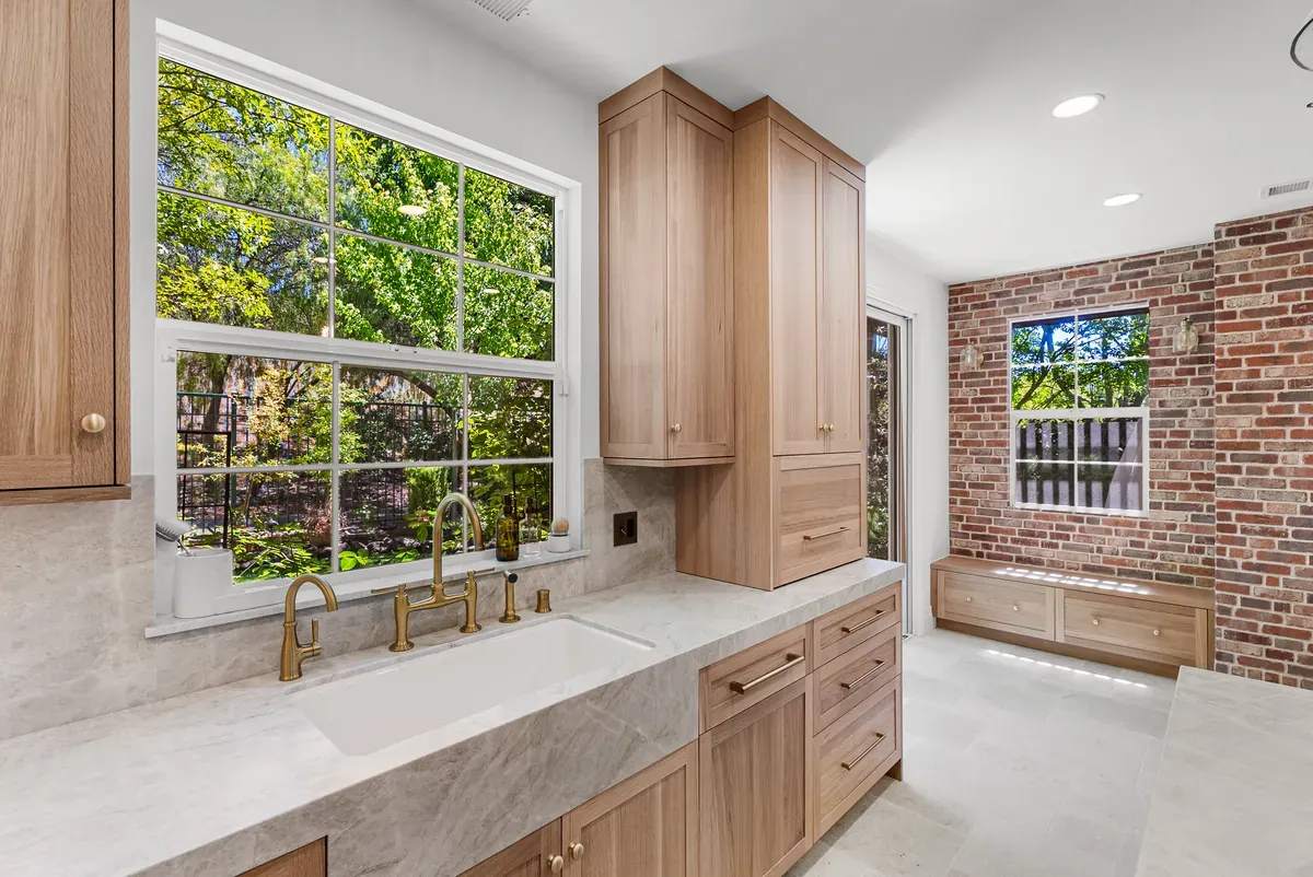 White oak kitchen run with marble counters, apron sink and a built-in window bench against exposed brick