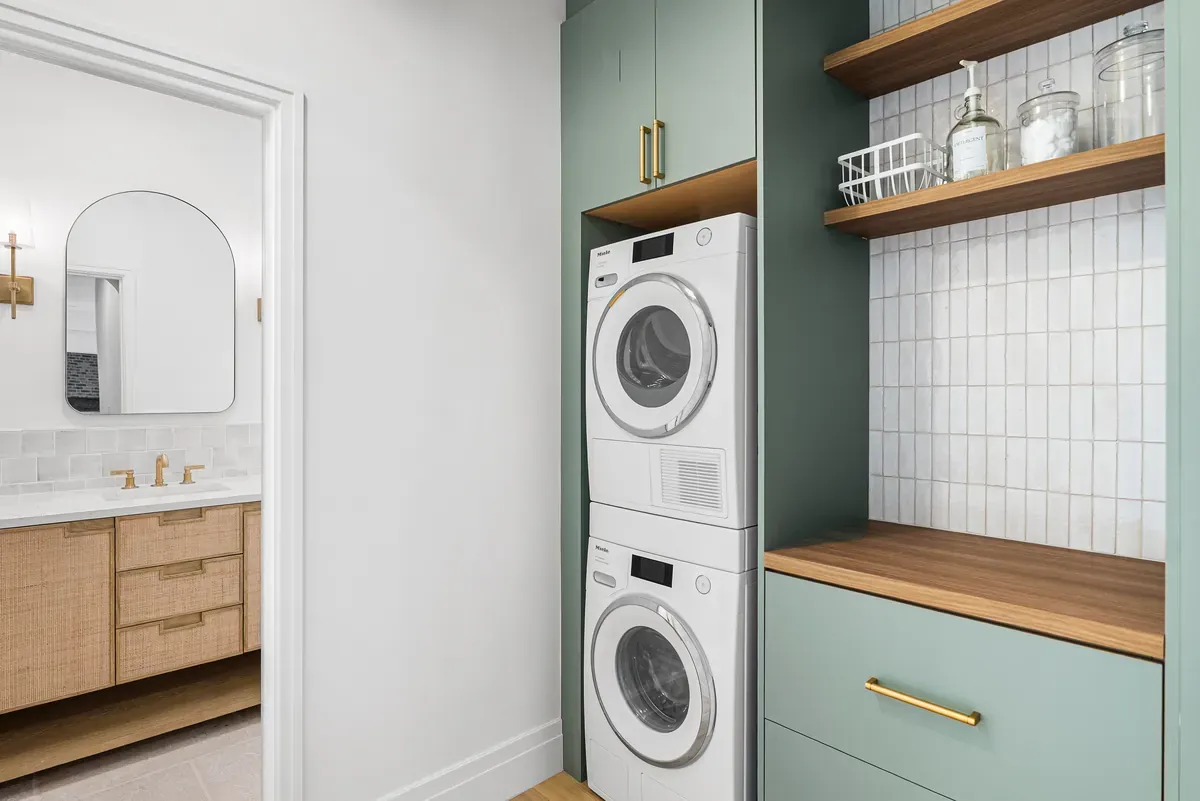 Laundry room with sage green cabinetry, stacked washer dryer and oak shelving