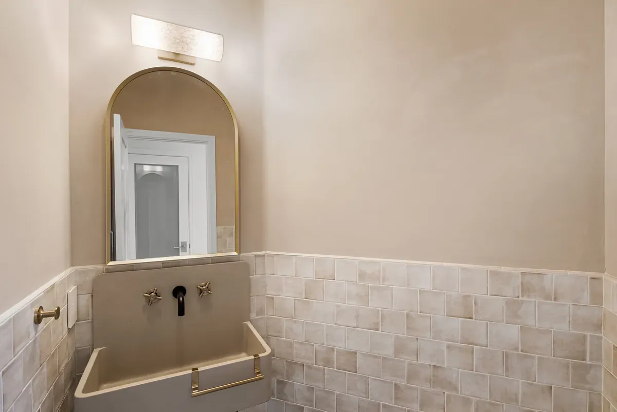 Powder bath with arched mirror, wall-mount brass faucet and handmade tile wainscot