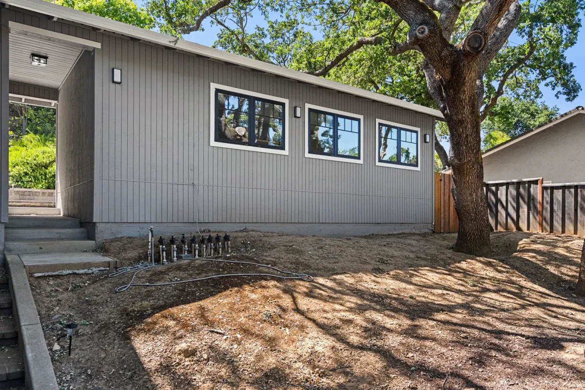 Grey board-and-batten JADU under a mature oak, with a row of clerestory windows