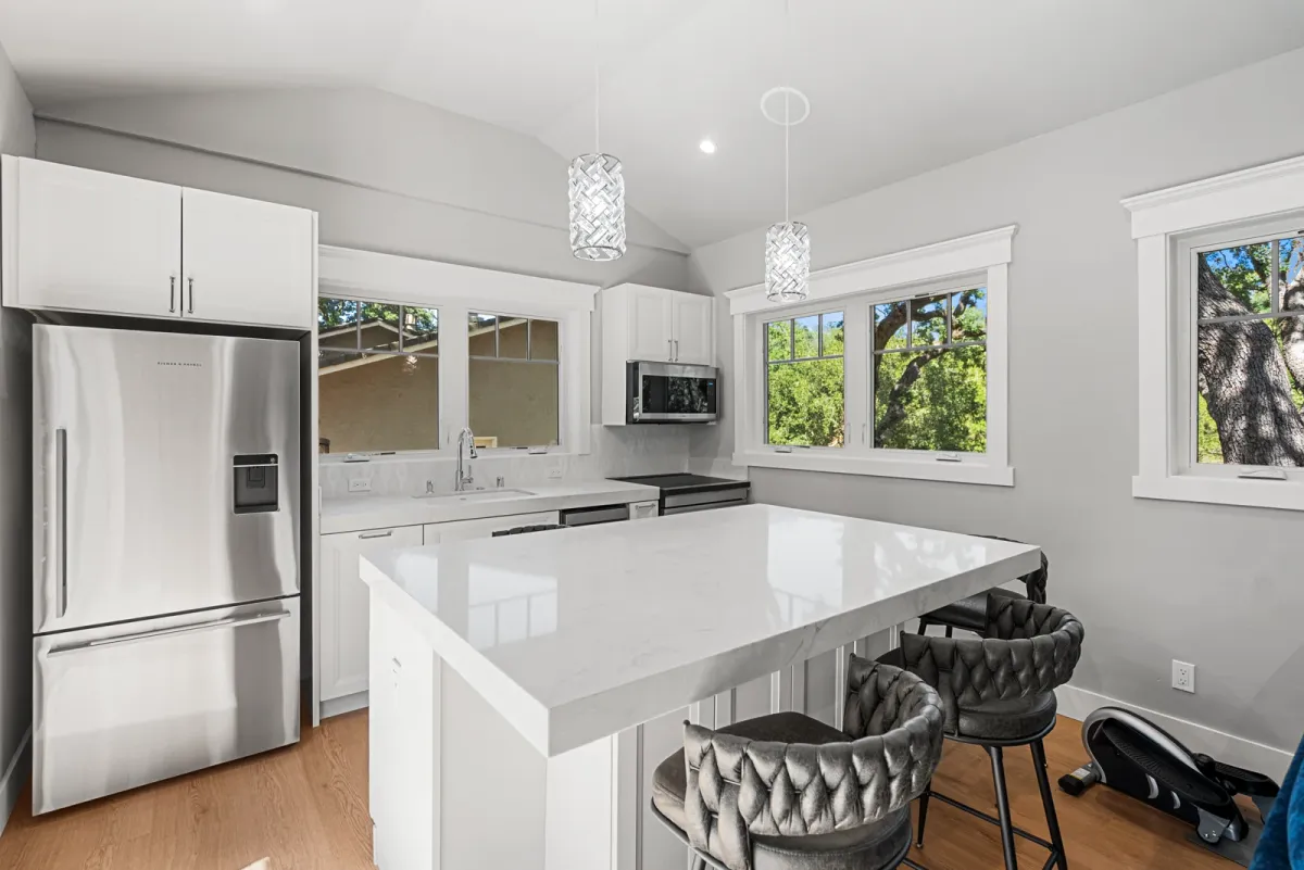 White kitchen with a quartz island, two stools, refrigerator and a glass pendant