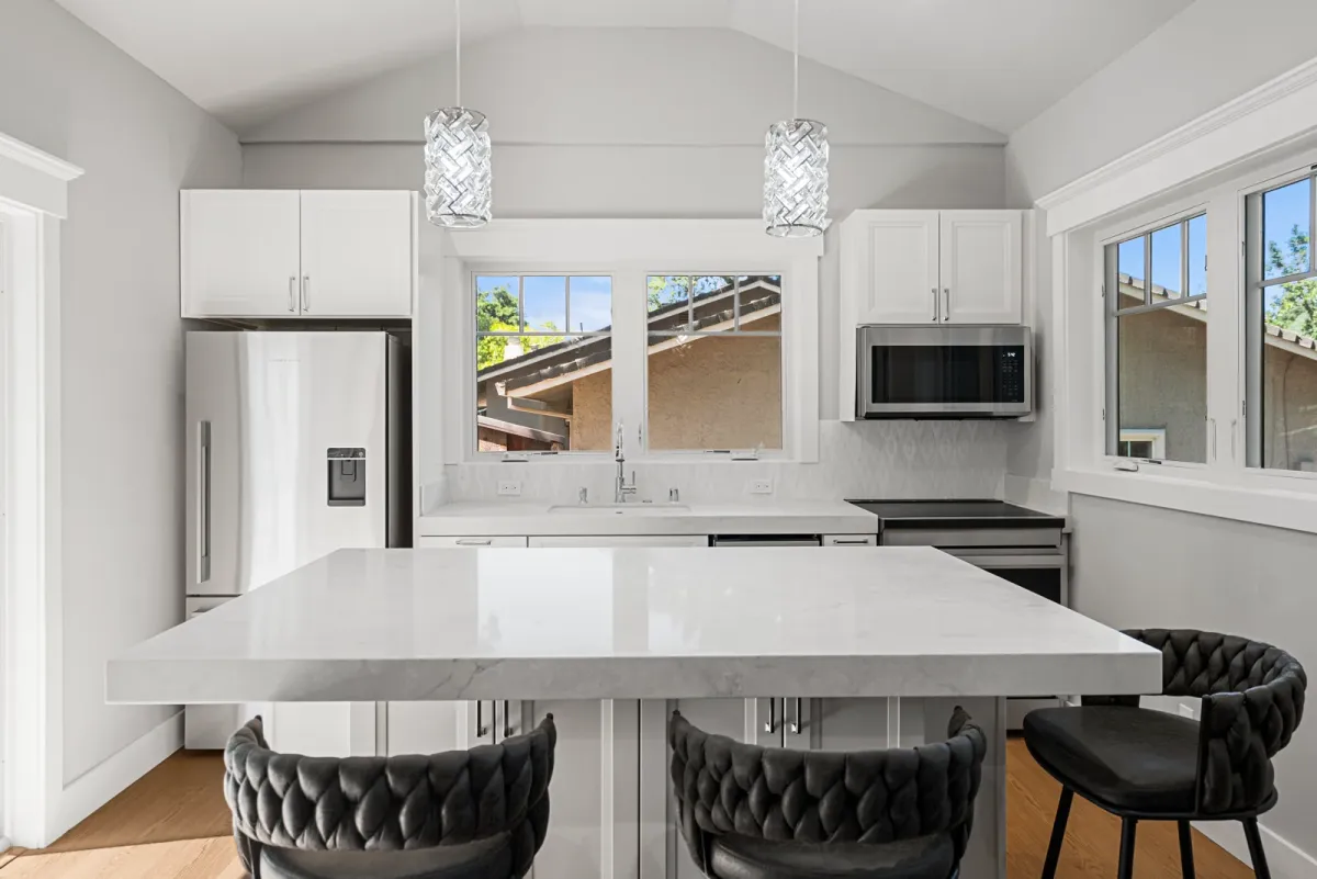 Kitchen island with three stools under glass pendants, range and refrigerator behind