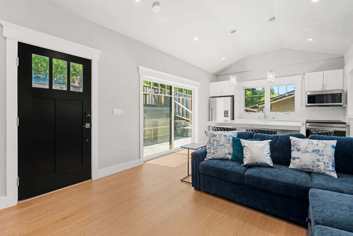 Black front door and sliding door beside the navy sectional, with the kitchen beyond