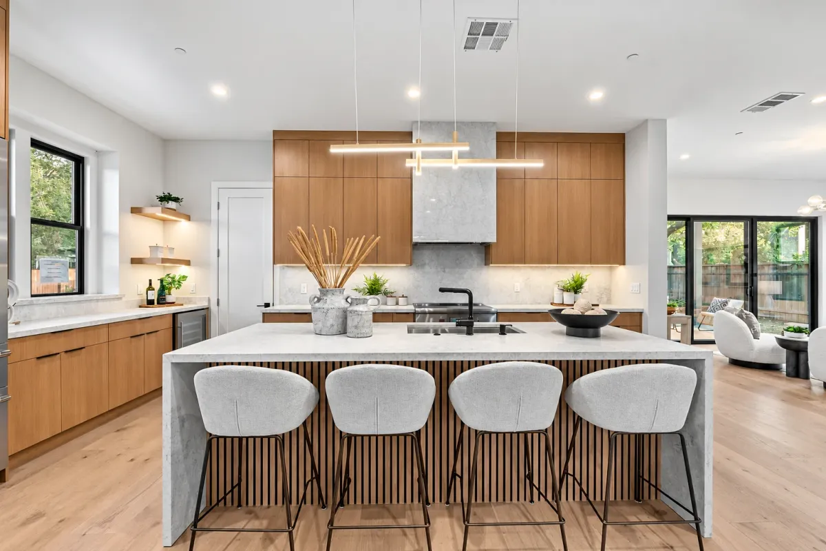 Kitchen island with four counter stools under a linear pendant, fluted white oak island base
