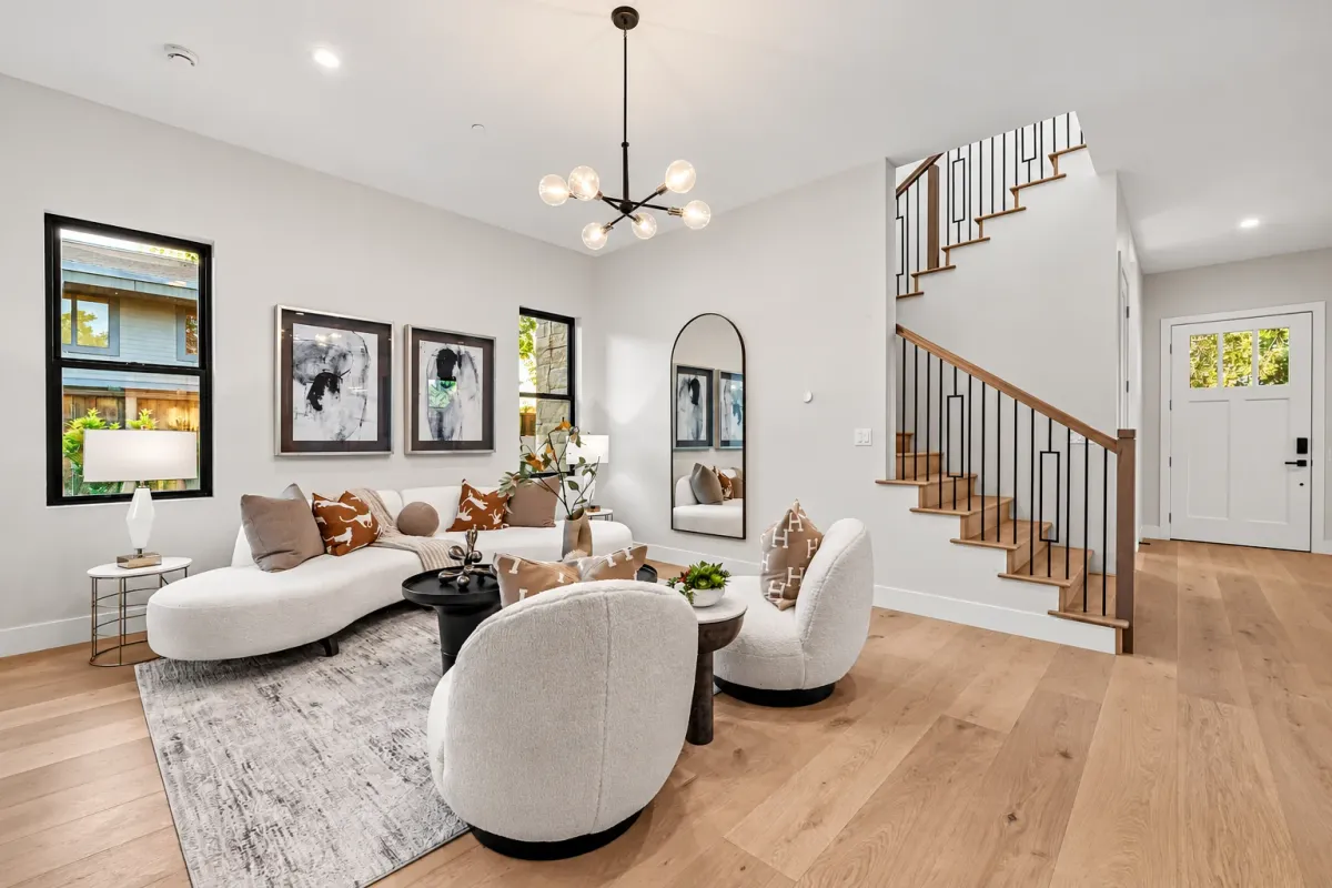 Living room with a curved sofa, black chandelier and framed art beside the staircase