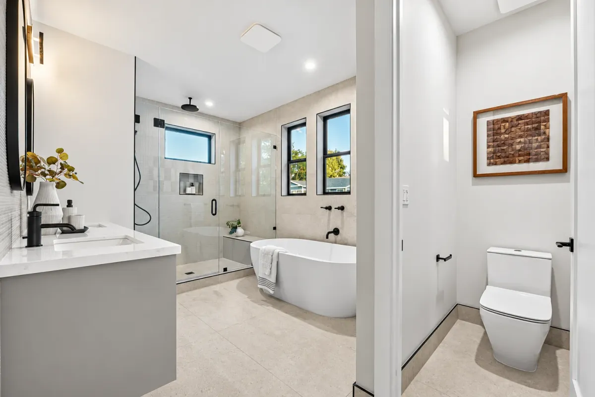 Primary bath vanity with matte black fixtures, the tub and a separate toilet room beyond