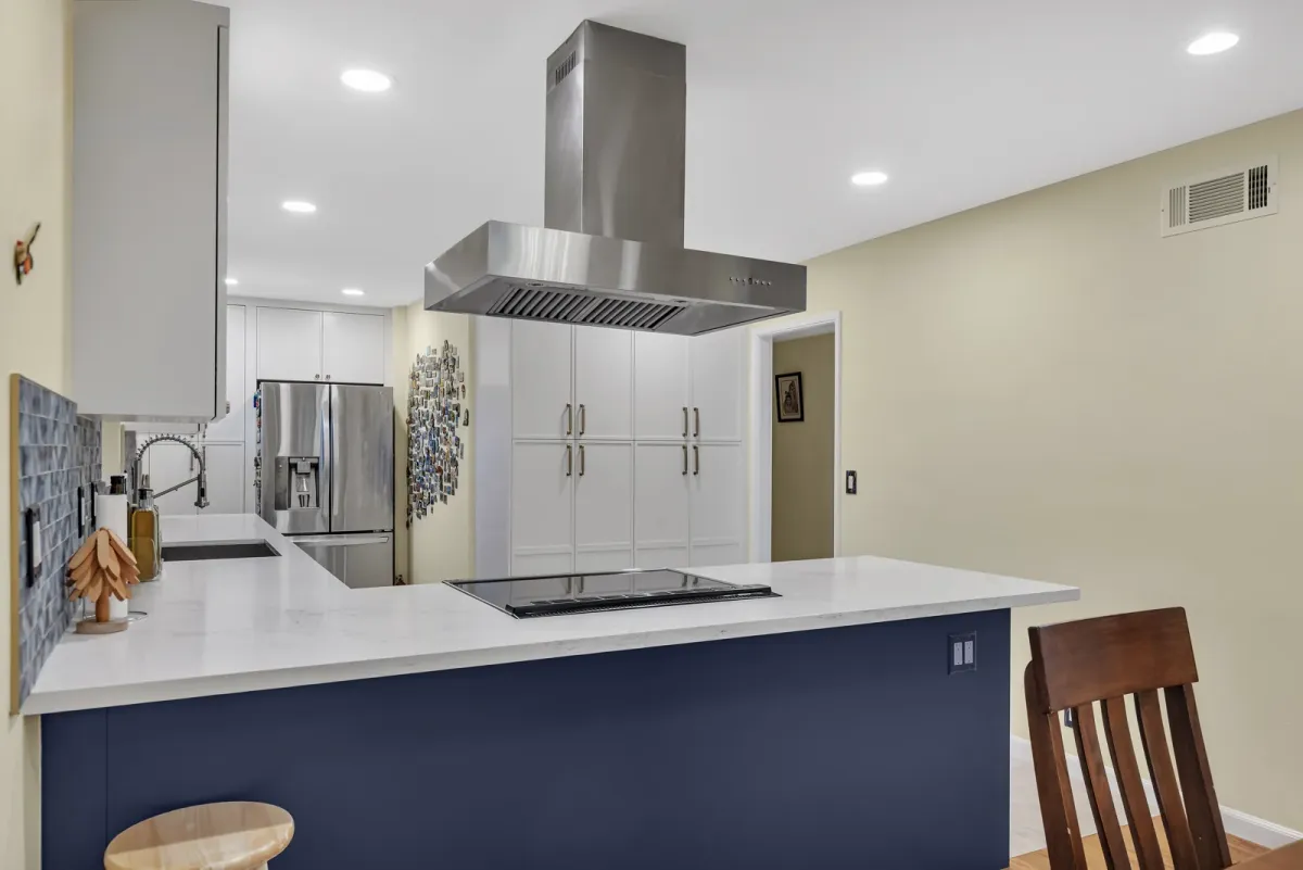 Floor-to-ceiling white pantry cabinets beside the refrigerator, navy base cabinets and quartz counters